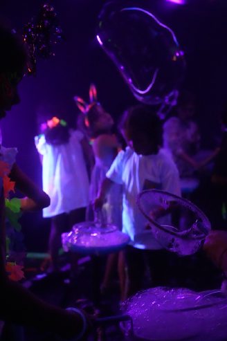 Niños jugando con burbujas gigantes bajo luz negra
