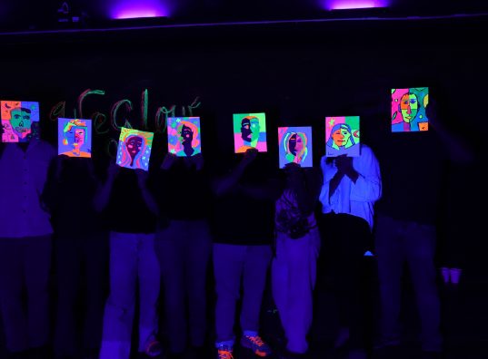 Asistentes mostrando sus cuadros bajo luz negra al cierre del taller