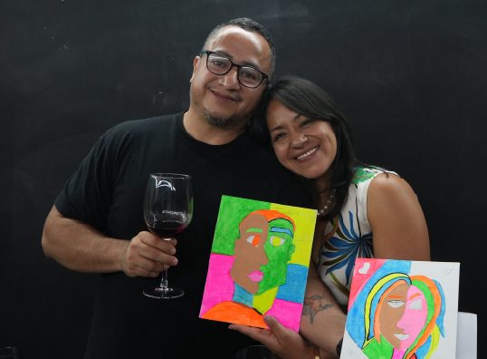 Pareja con sus cuadros terminados y una copa de vino al cierre del taller